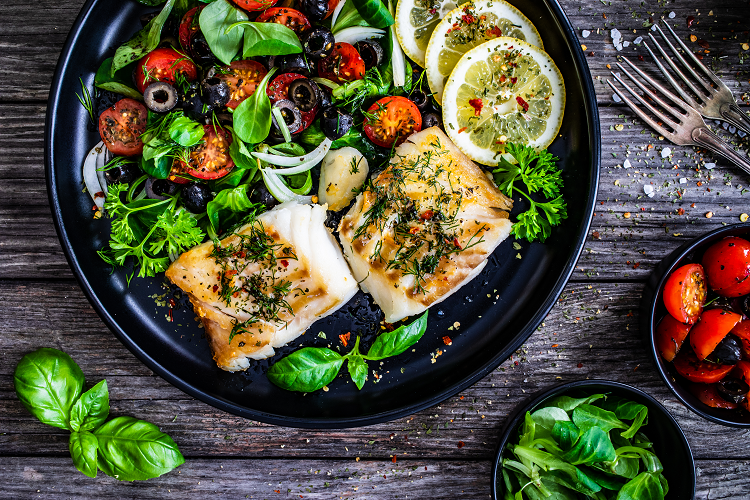 Grilled fish on a plate with salad and lemon slices